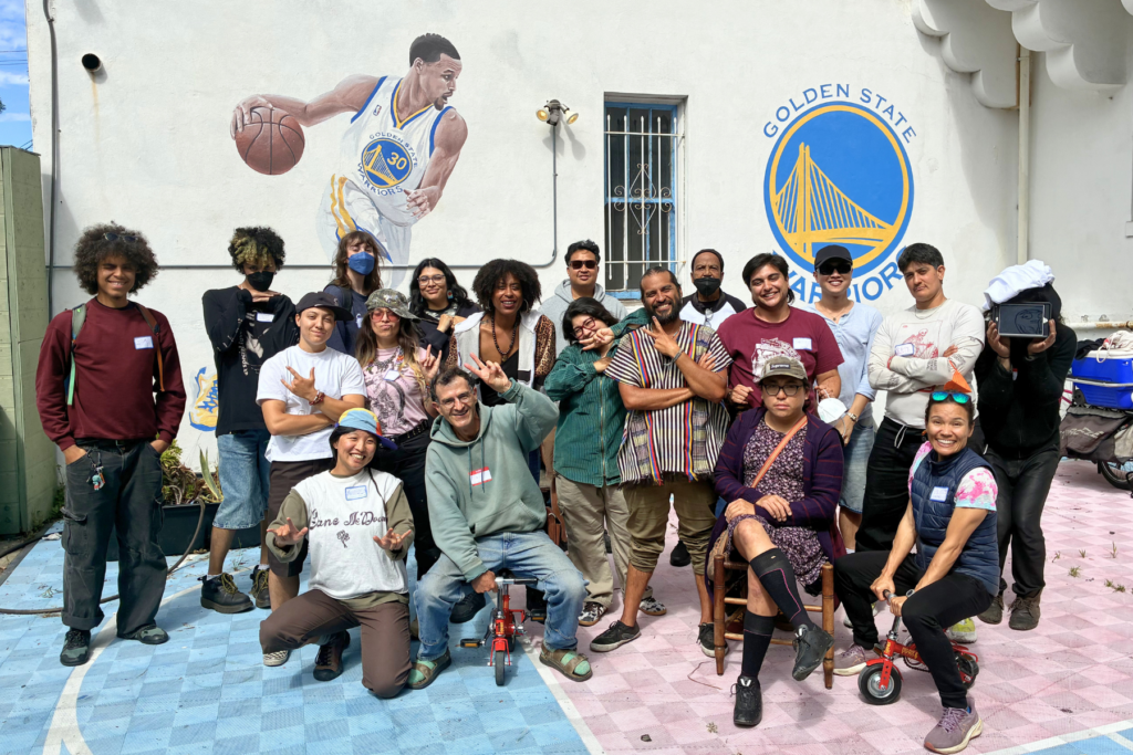 A group of smiling black and brown adults in front of a mural of Steph Curry.